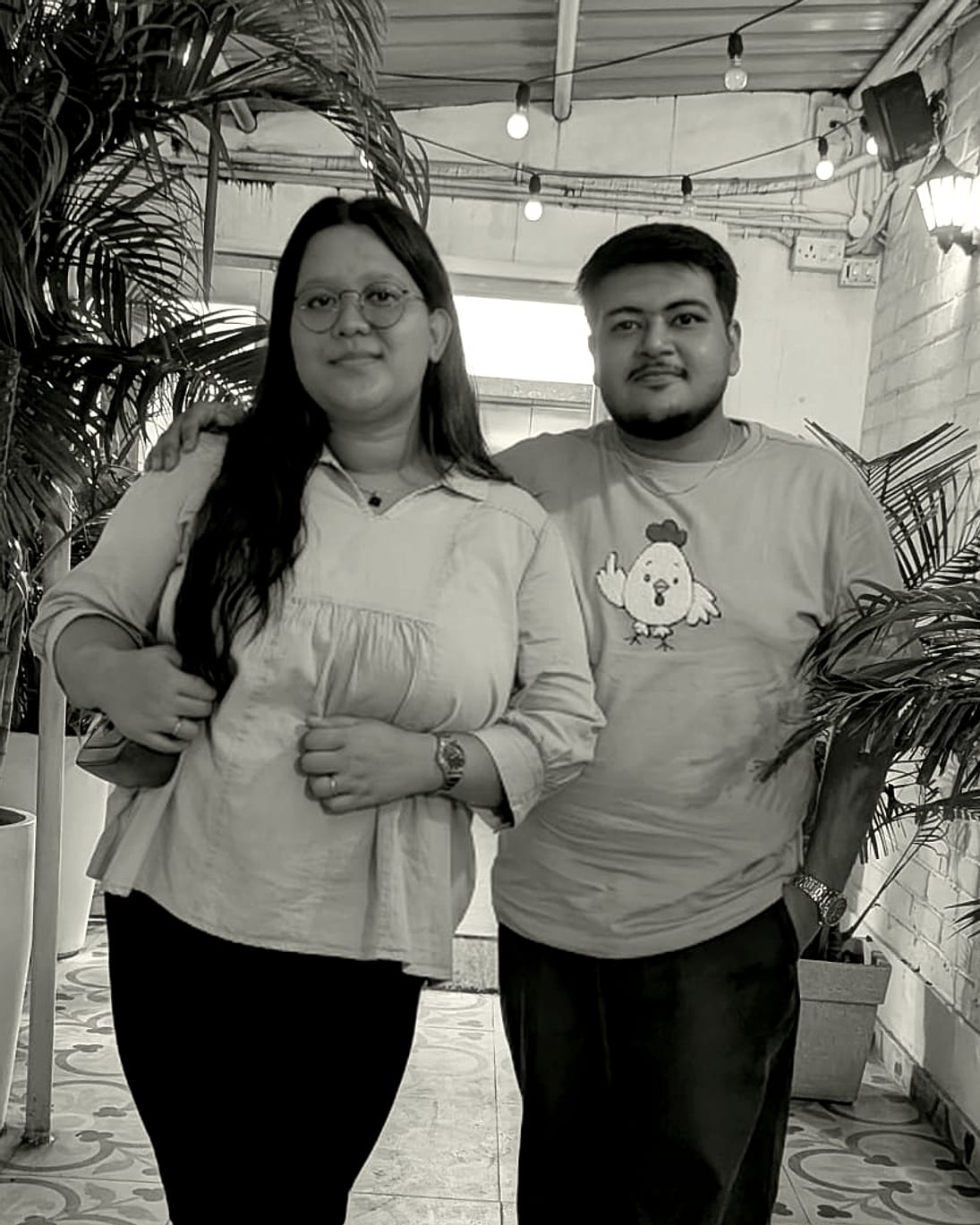 Rachel and Praduan on a plant-filled terrace beneath string lights
